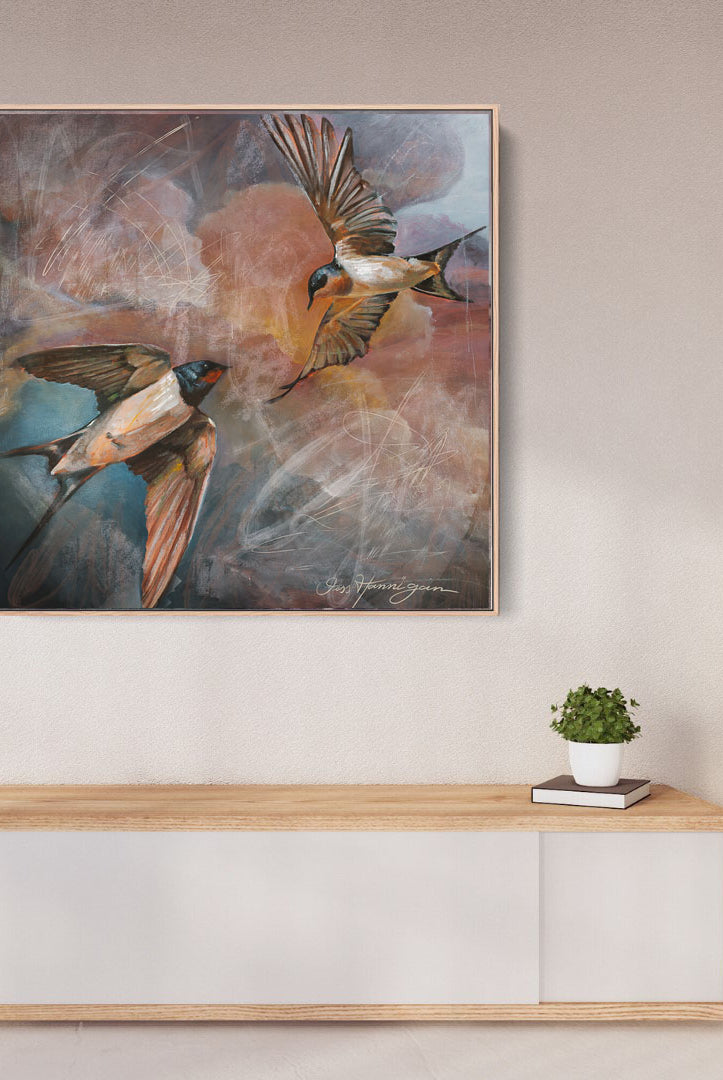 Framed artwork of birds on a wall above a wooden console table with plants.