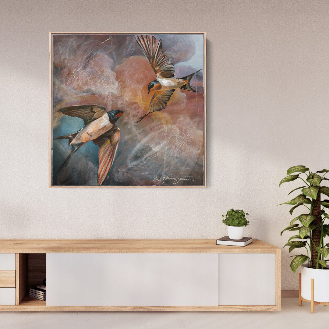 Framed artwork of birds on a wall above a wooden console table with plants.